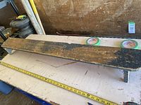 Shows length of plant stand with worn dark wood finish and attached short legs.