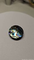 Round abalone doublet gemstone placed on a white surface showing natural iridescent colors and patterns under natural light.
