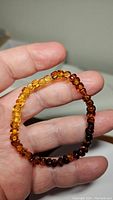 Photo showing natural Baltic amber bracelet held in hand, displaying the gradient colors of amber beads from light yellow to dark brown, the free-form cube shapes are clearly visible.