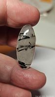 Close-up photo of oval cabochon black rutilated quartz held between fingers showing the inclusions and clarity