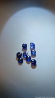 Seven natural round blue sapphire cabochons displayed on white surface under focused light showing deep blue color and shine.
