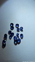 Multiple small natural blue sapphires on a white background showing denim blue color and round cut.