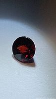Photo of a single round fancy cut deep red almandine garnet showing its facets and deep color under directional lighting.