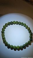Photo of a natural green jade bead bracelet arranged in a circular shape showing the round polished beads under lighting.
