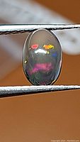 Close-up image of oval cabochon Ethiopian black opal with multicolored flashes including orange, red, yellow, and pink on dark body.