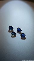Four blue sapphire gemstones on white background, mixed oval and pear cut shapes, showing color and surface details