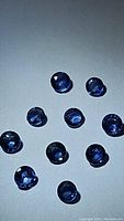 Multiple natural blue round sapphires on a white background, showing size and color.