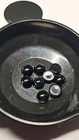 Nine small round black onyx cabochon stones in a black dish, showing their glossy polished surface and consistent color.