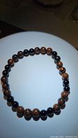 Photo of stretched natural mahogany jasper bracelet with polished round brown and black beads on white background.