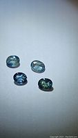 Four oval-cut multicolored sapphires displayed on a neutral background showing color variation from blue to green