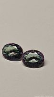 Pair of oval cut mystic topaz gemstones on plain background showing color and cut.