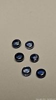 Six natural blue sapphire round cabochon gemstones laid out on a flat beige surface.