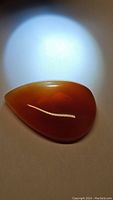 Large pear-shaped deep orange carnelian gemstone cabochon with smooth polished surface under focused lighting