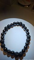 View of the natural gemstone bracelet showing alternating black lava stone and hematite beads on a white circular display.