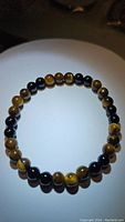 Single stretchy bracelet made of alternating natural yellow tiger's eye and black onyx 6mm beads laid flat in a circle.