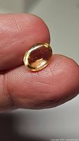 Close-up photo of natural oval cabochon golden citrine gemstone held between fingers showing smooth surface and golden color.
