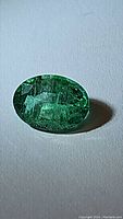 Close-up of natural oval cut emerald showing green color and internal inclusions under lighting
