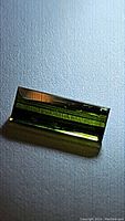 Close-up photo of rectangular baguette cut green tourmaline gemstone on light textured background showing natural clarity and color.