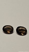 Pair of natural smokey quartz faceted oval cut gemstones side by side on white background.