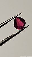 Close-up view of the pear-shaped natural ruby held by tweezers, showing deep red color and natural inclusions.