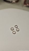 Photo showing four small silver jump rings on a neutral background.