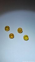 Four loose round cut natural yellow sapphire gemstones placed on a plain background showing size and color consistency.