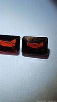 Two rectangular deep red garnet gemstones shown under light, highlighting their emerald cut and clarity.