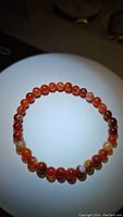 Top view of natural red agate bracelet showing round polished 6mm beads with varied banded patterns in red, orange, white, and brown hues, on stretchy elastic cord.