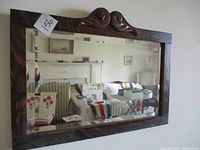 Full frontal view of antique rectangular mirror in tiger oak frame with carved scroll detail on top and beveled glass reflecting room interior.