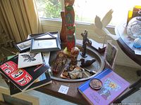 Wide view showing multiple items on a circular table: totem pole, books, figurines, doll, artwork, ceramic dish