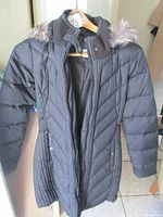 Full view of the black quilted winter coat with fur-trimmed hood, hanging on a wooden hanger.