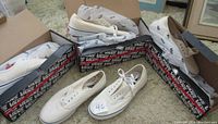 Four pairs of white Vans Off The Wall classic lace-up shoes, three pairs in original Vans boxes and one pair loose, displayed together.