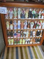 Full frontal view of the wooden display case filled with rows of glazed ceramic figurines depicting traditional peoples in cultural costume.
