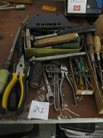 Photo showing multiple hand tools including yellow-handled pliers, wooden hammer, wrenches, files, and screwdrivers laid out on surface.