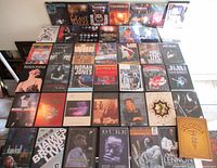 Top view of all DVDs and CDs arranged in rows on the floor, showing a variety of music concert recordings and live performance videos and audio CDs.