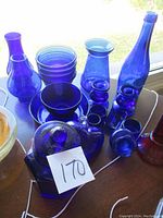 Collection of blue glass items including bowls, bottles, jars, and candle holders with a visible lot number 170 on a white card.