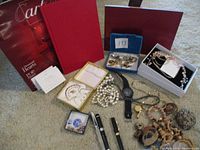 Wide view of lot showing Cartier booklets, fountain pens, pearl necklace, watch, assorted jewelry and hairpiece.
