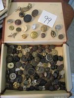 Top view of open box showing a variety of vintage and military buttons arranged on a folder and loose inside the box