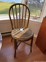 Front view of bamboo dining chair showing curved vertical back slats and woven round seat, positioned by window with natural light.