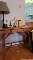 Full view of bamboo desk with lamp and items on top, shows knocker drawer front and woven detail on top surface