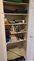 Closet shelves with stacks of folded wool and fleece blankets, bed linens, bath towels, vanity set, seat cushions, and two irons visible.