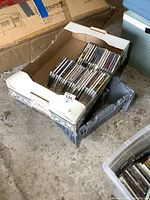 Two boxes of CDs stacked in an area with some dirt and boxes around them, showing quantity and storage condition