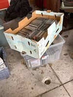 Box filled with rows of CD jewel cases and paper sleeve with mixed genre CDs.