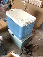 Two stacked powered coolers on floor, one blue Igloo on top and one green Koolatron below with power cord visible.