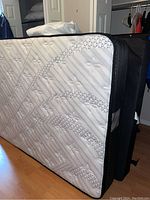 Mattress and boxspring leaning against black metal frame in bedroom