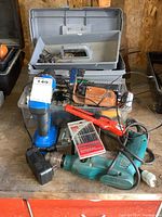 Makita corded drill, Mastercraft cordless drill, plastic toolbox, drill bits, utility knife and charger displayed on wooden surface