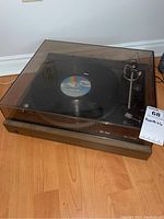 Front angle view of the complete Dual 506 turntable showing wood veneer base and plastic cover with a record on the platter.