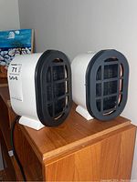 Pair of white micro space heaters placed on a wooden surface showing front and side views.