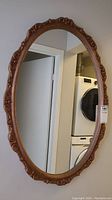 Full view of the oval wall mirror showing its copper resin frame and reflective surface against a wall near a laundry area.