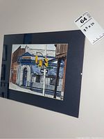 Angled view of the matted painting on the wall with auction sticker visible